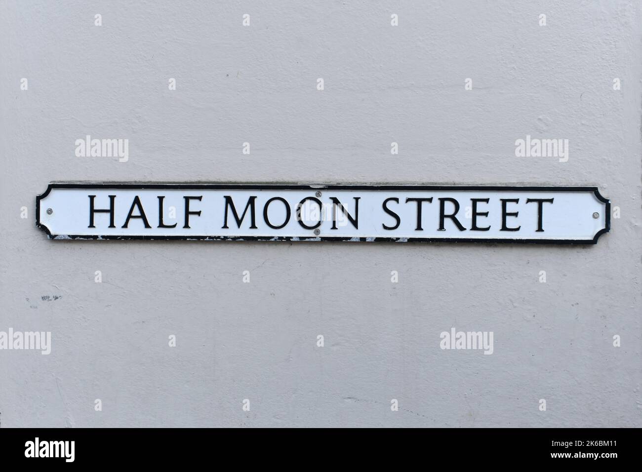 close up of street name plate,  Half Moon Street, on an old grey painted wall background.  The vintage text sign is written in black on a white metal Stock Photo