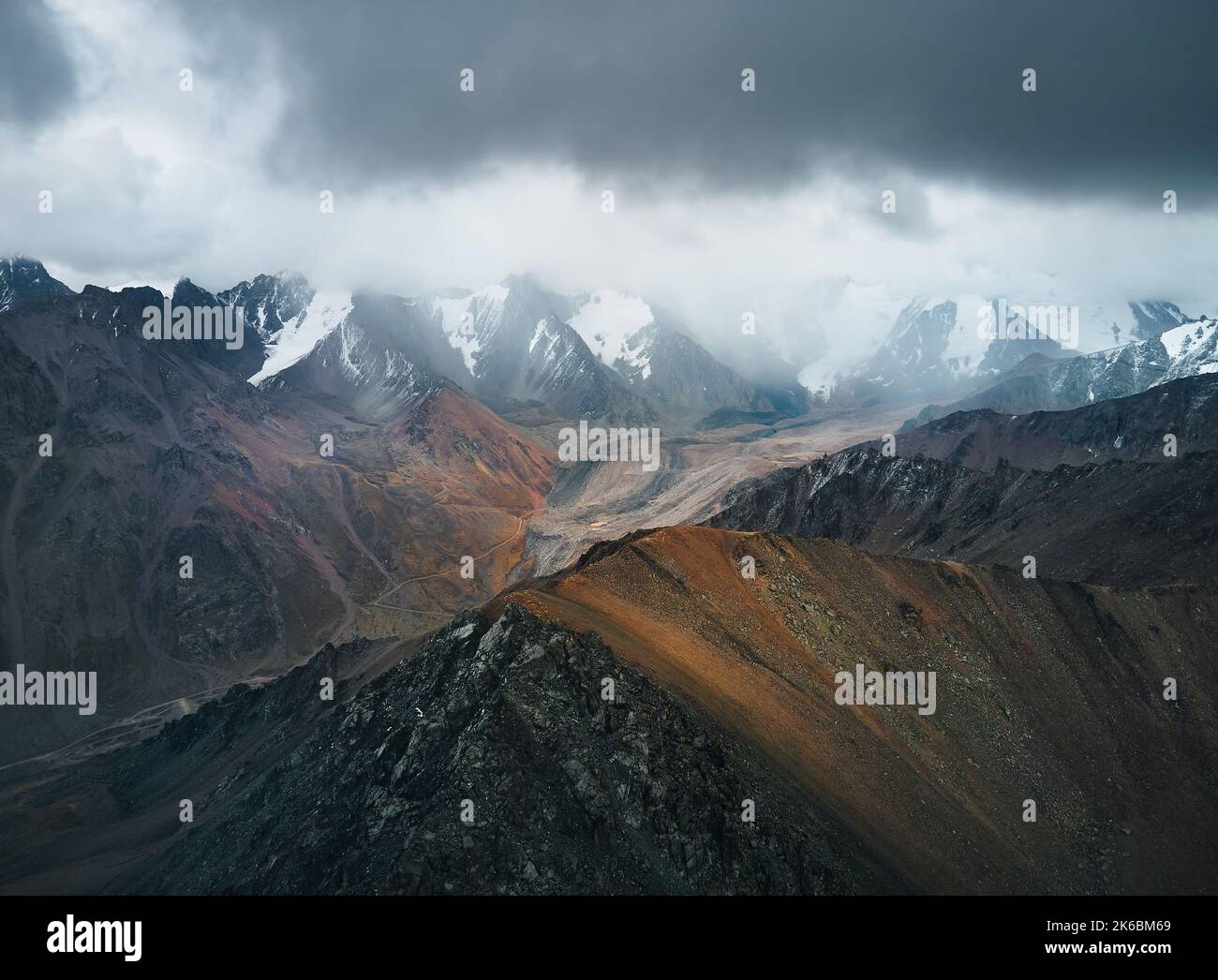 Aerial drone landscape shot of snow summit with ice glacier and and rocky wall at mountain valley with cloudy dark sky in Kazakhstan Stock Photo