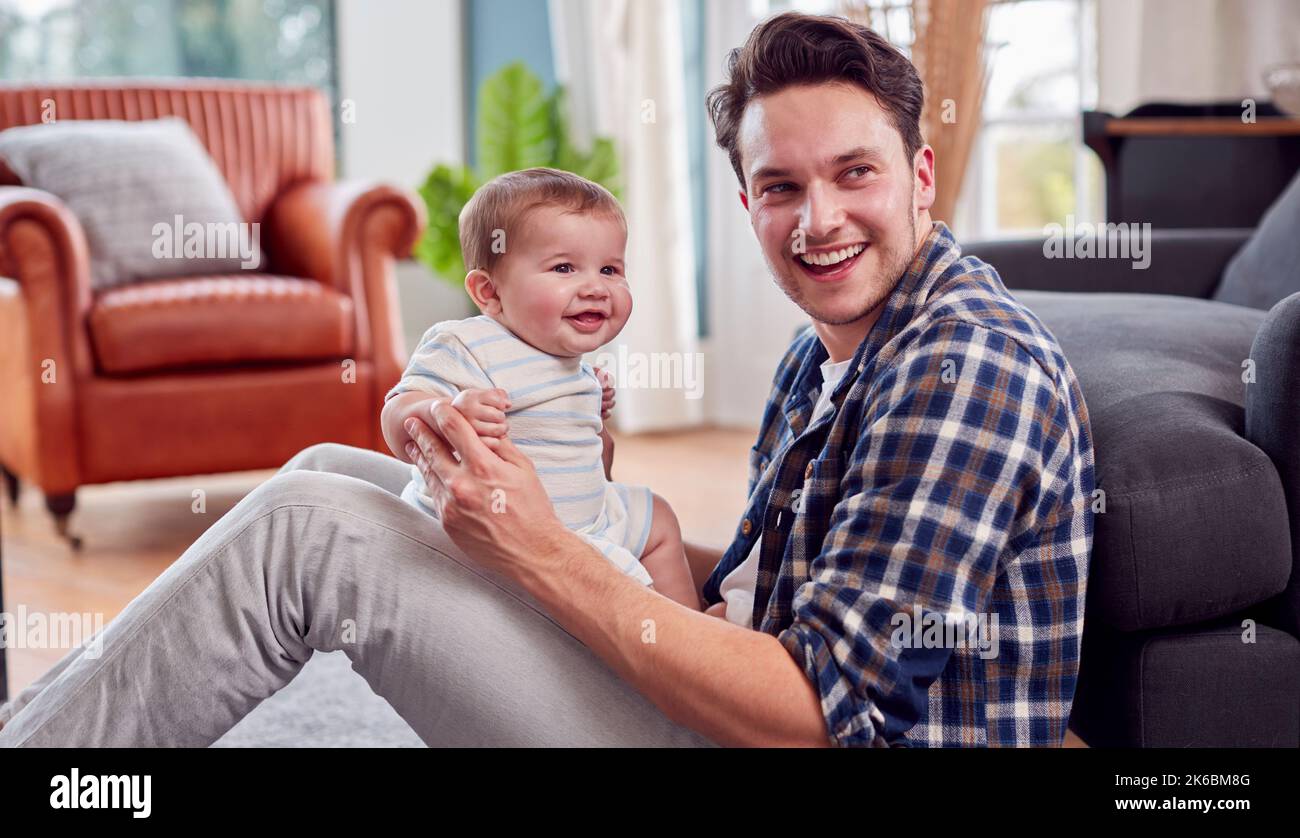 Loving Transgender Father Playing With Baby Son Sitting On Floor At Home Stock Photo