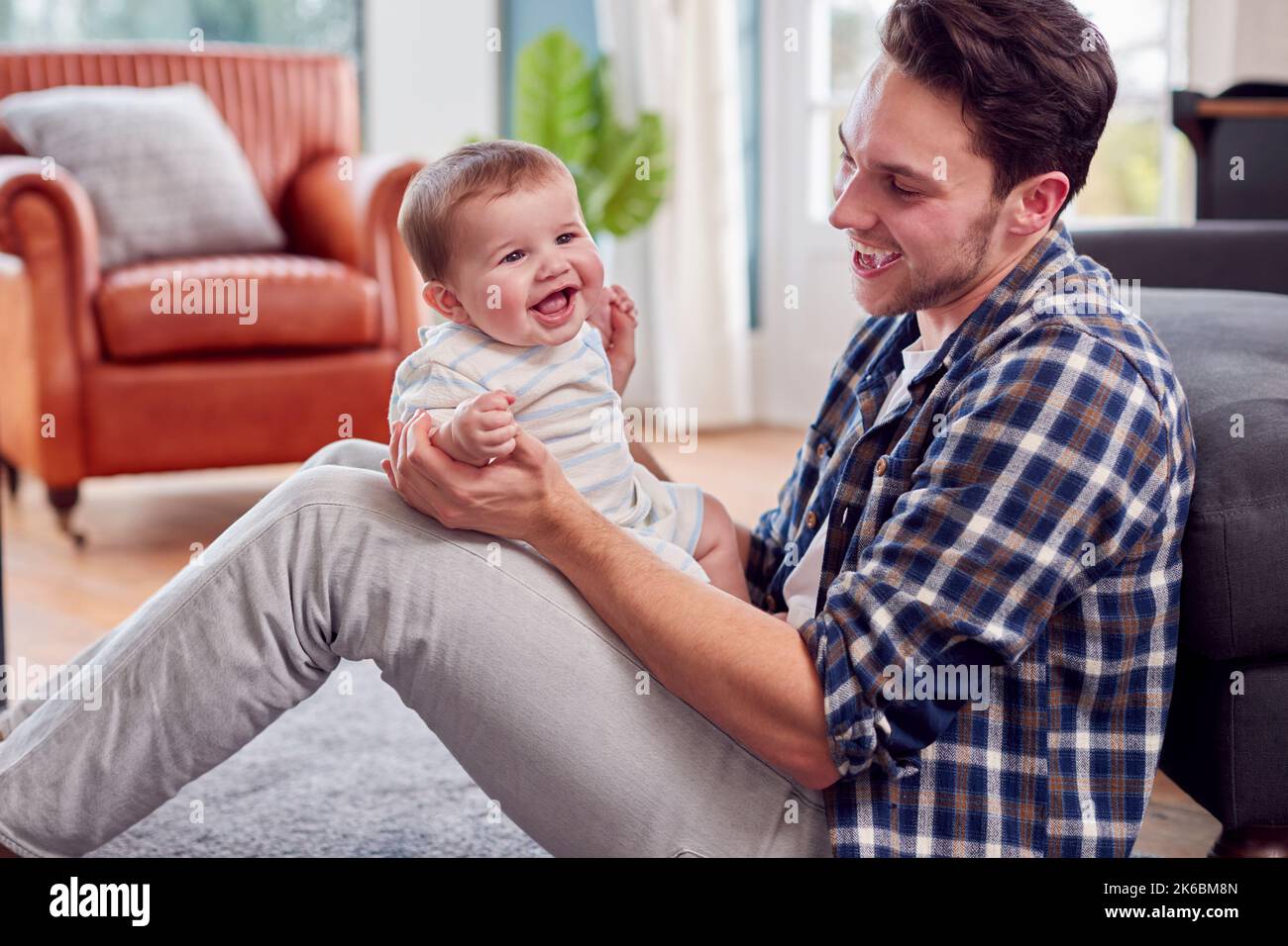 Loving Transgender Father Playing With Baby Son Sitting On Floor At Home Stock Photo