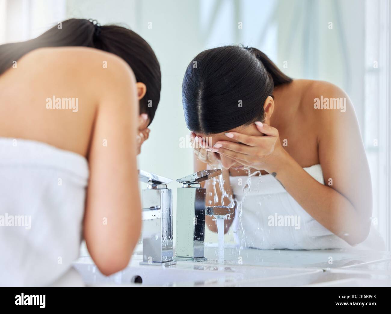 Wash it all away. a young woman washing her face in a bathroom at home. Stock Photo