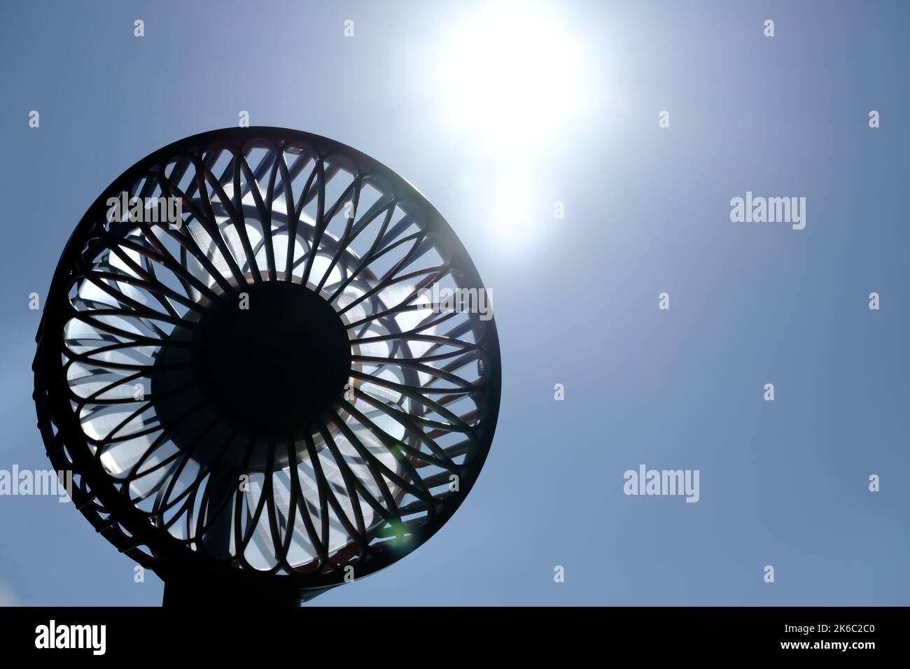 Handheld electric fan in silhouette under glaring summer sun with two