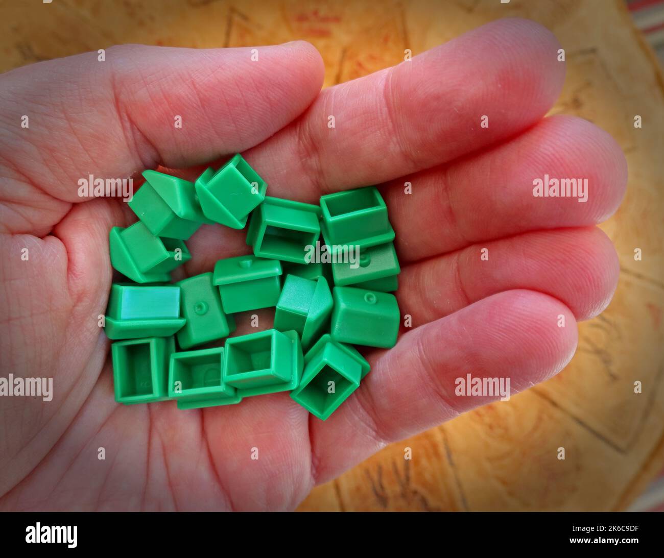 An adult hand, holding green Monopoly houses for rent or by, representing property and UK Housing issues Stock Photo