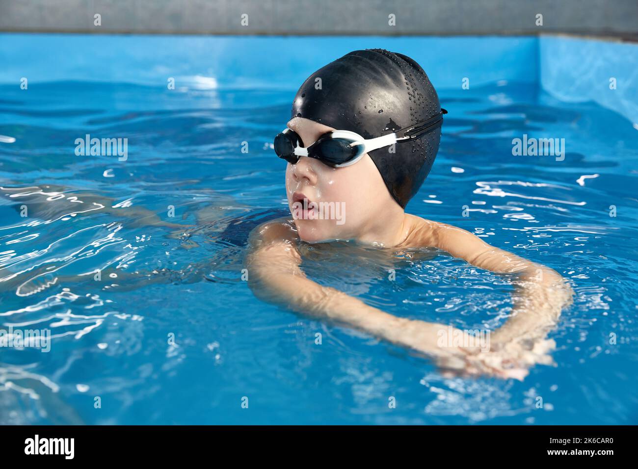 Preschool boy learning how to swim in a pool wearing swimming cap and