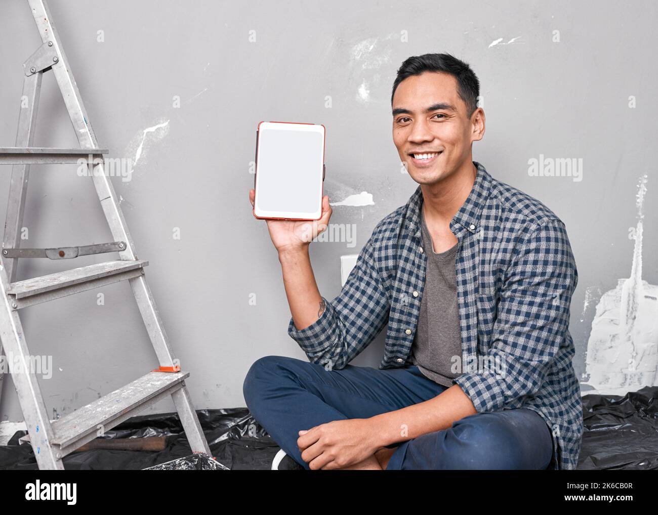 A young attractive Asian man holds up digital tablet doing home DIY improvement Stock Photo