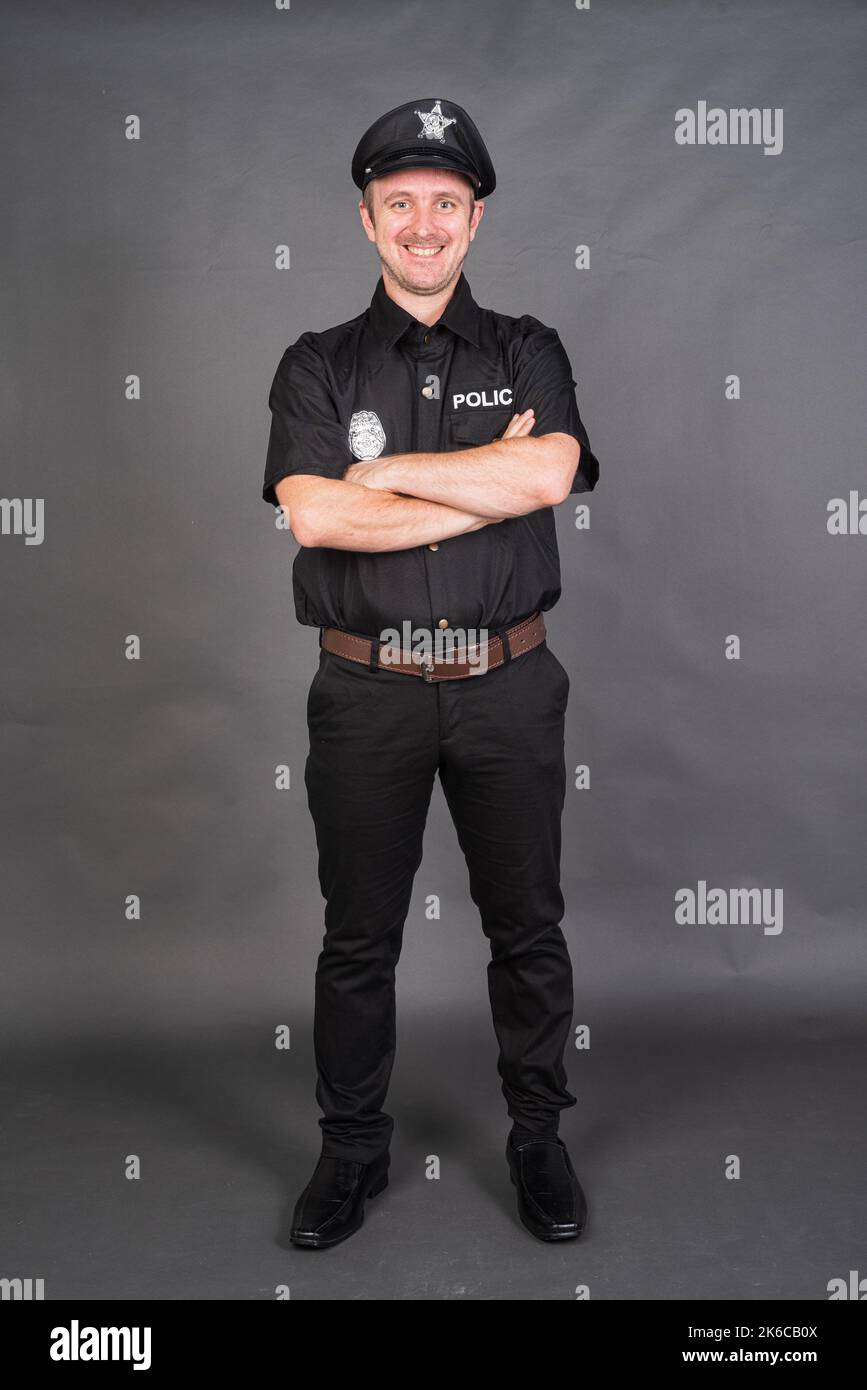 Portrait of Caucasian man wearing police uniform costume against gray studio background Stock Photo