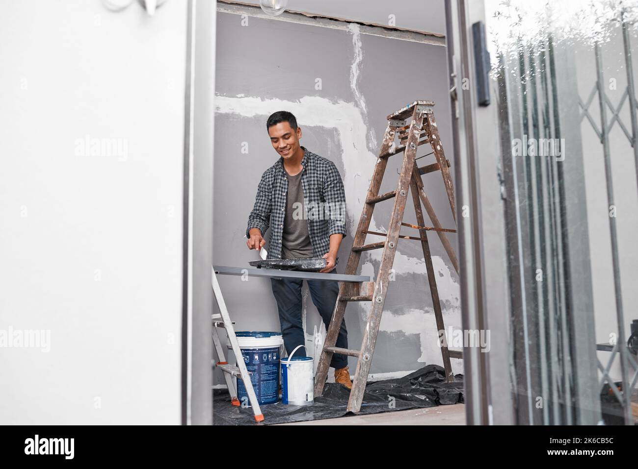 Ultra wide shot of Asian man painting a wall doing home renovation Stock Photo