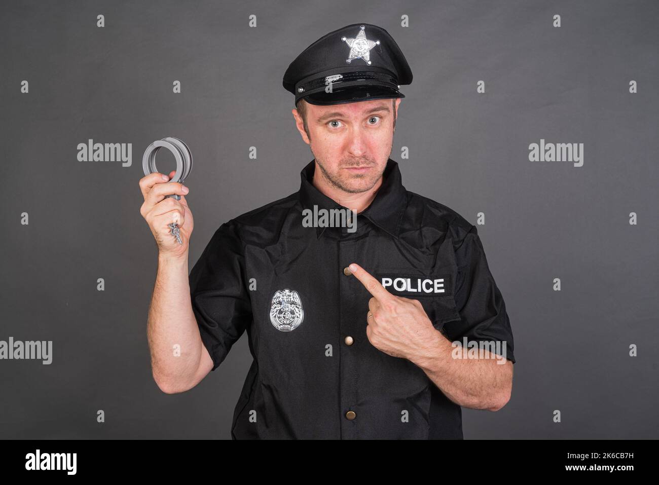 Portrait of Caucasian man wearing police uniform costume and holding handcuffs Stock Photo
