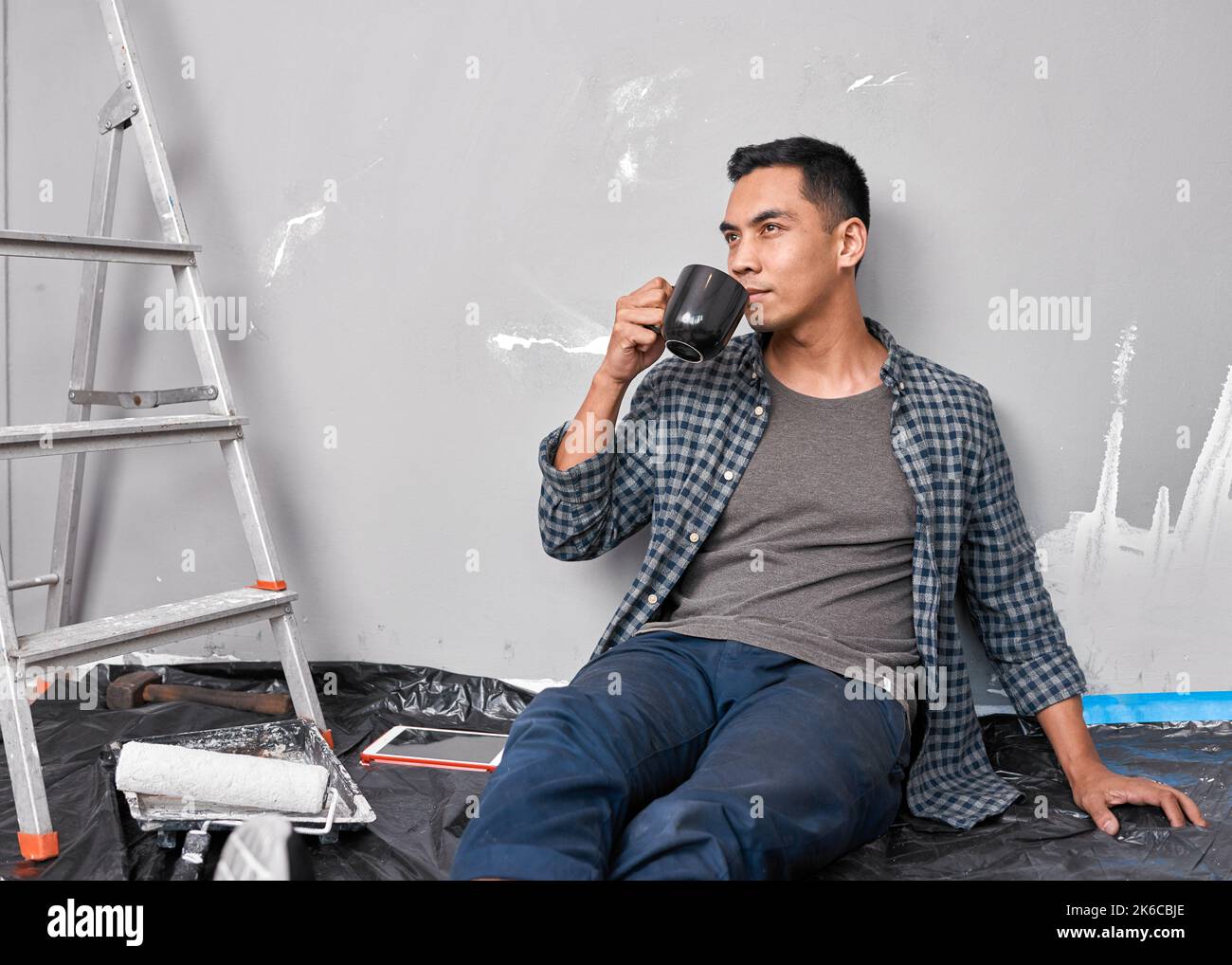 A young Asian man sips coffee while taking a break from home improvement DIY Stock Photo