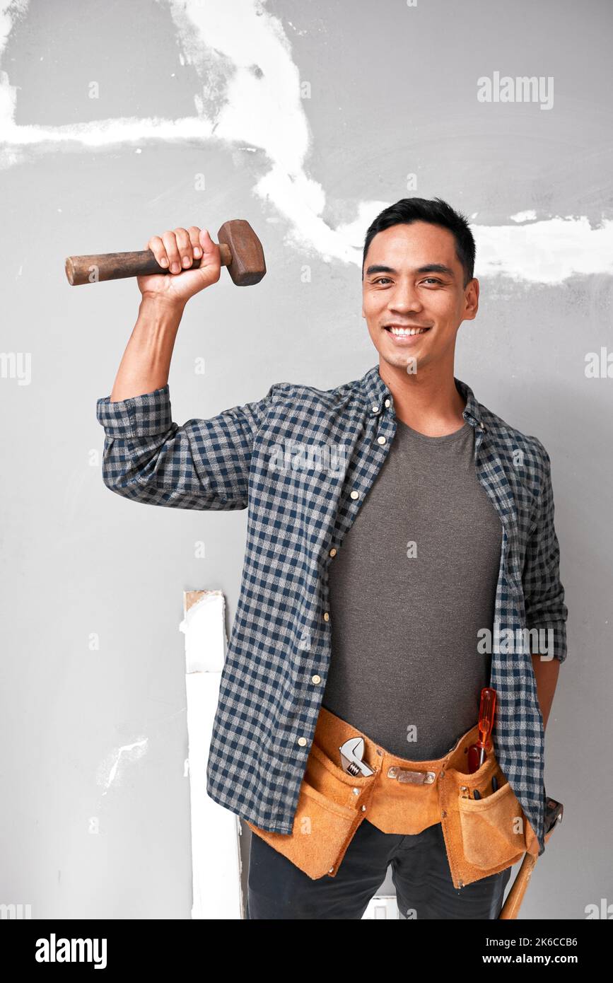 A young attractive Asian man holds up a mallet with strong arm doing home DIY Stock Photo