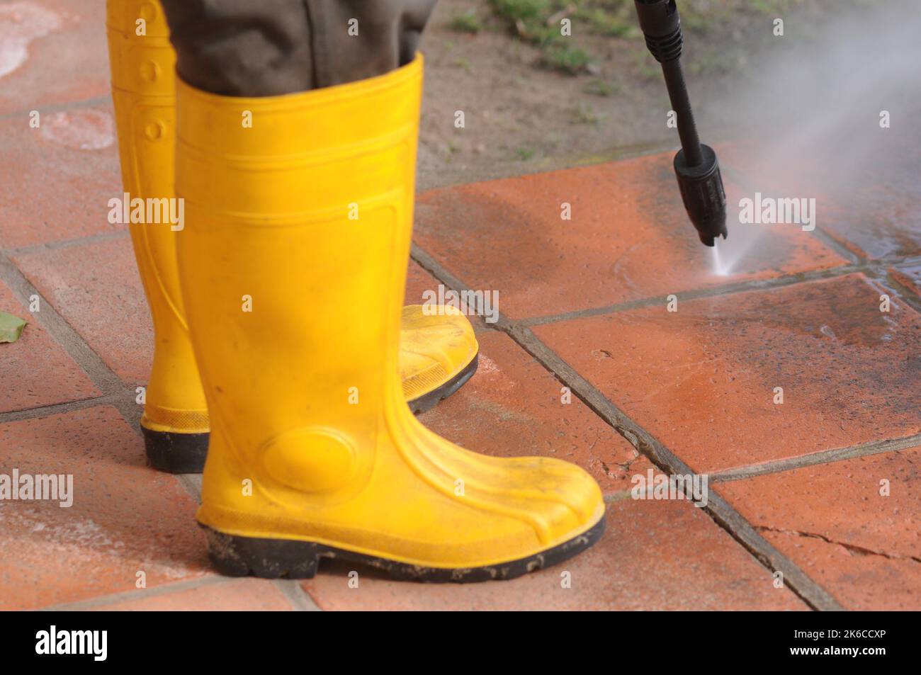 Person wearing yellow rubber boots with highpressure water nozzle cleaning the dirt in the