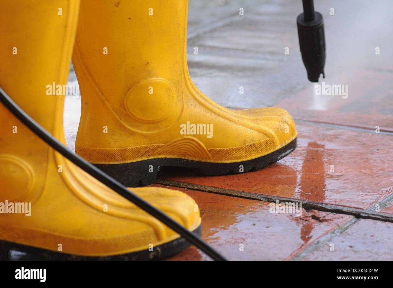 Person wearing yellow rubber boots with highpressure water nozzle cleaning the dirt in the