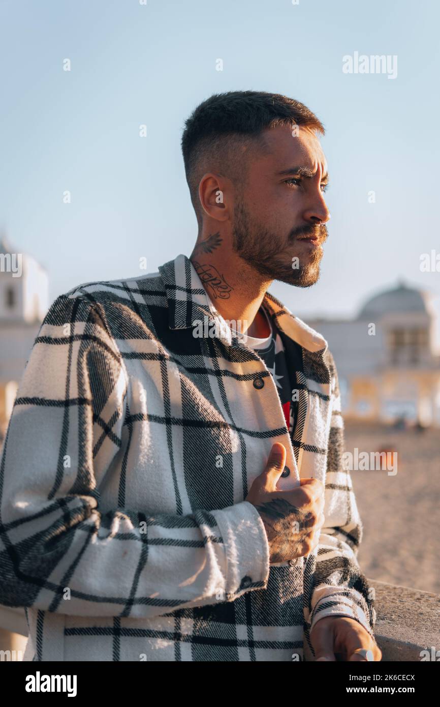 A portrait of a Caucasian model young man in a plaid jacket and earring with blur beach Stock Photo