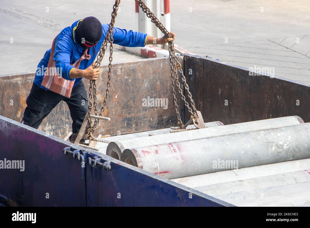 A worker attaches chains from a crane to concrete tubes on the load space of a truck Stock Photo