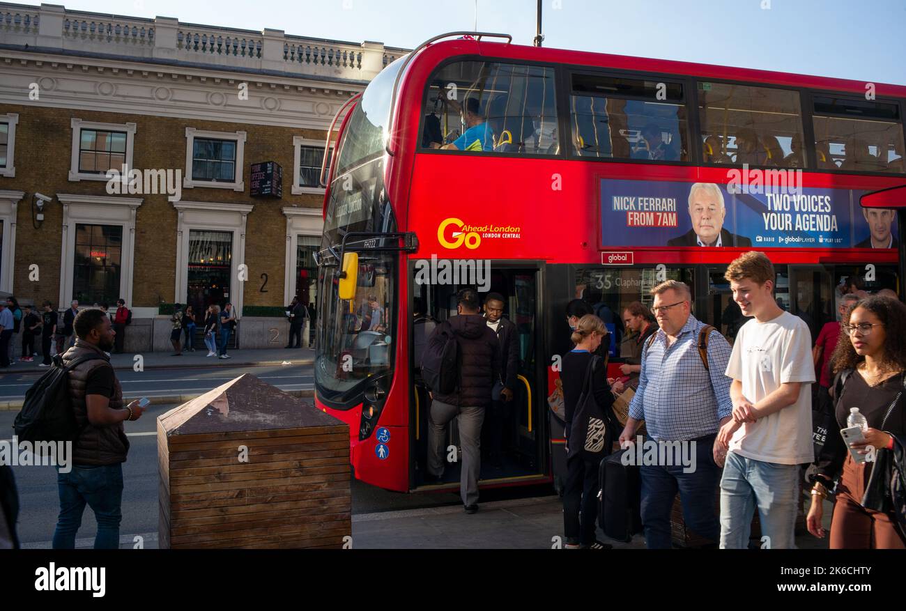 London city life captured in street photography style. Passenger alight from red bus as commuters pass by caught in evening sun. Stock Photo