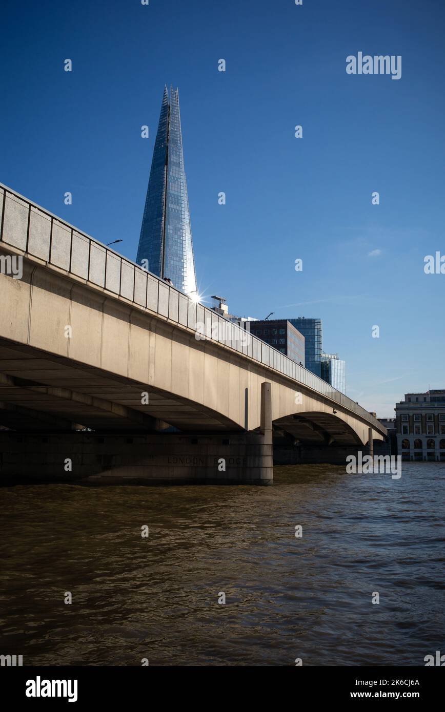 London Bridge and river Thames in the foreground bathed in sunshine with the Shard above with light reflecting off in a London upright landscape. Stock Photo