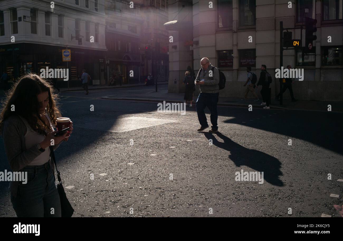Members of public distracted by their mobile phones why walking across road  in London in evening light. Stock Photo