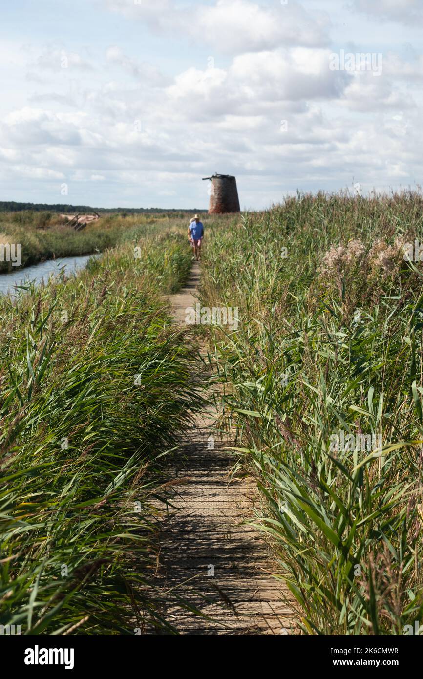Person walking along bankside trail  near old widnd pump windmill on the River Dunwich near Walberswick in Suffok England Stock Photo