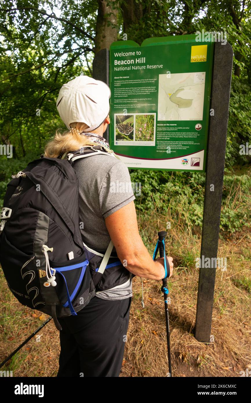 Lady hiker with rucksack and walking poles looking at sign on Beacon Hill along the South downs Way near Winchester Hampshire England Stock Photo