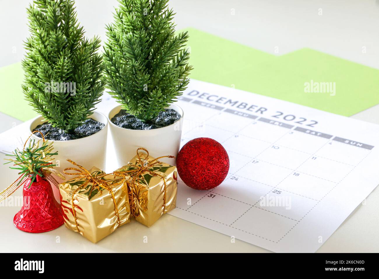 Christmas concept, festive decor, two pine tree plants, two gold wrapped gifts, a shiny red bell, and a red bauble, on December calendar Stock Photo