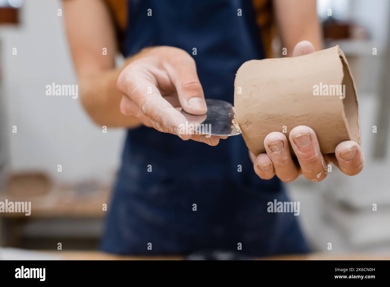 Cropped view of sculptor forming clay product with steel scraper in