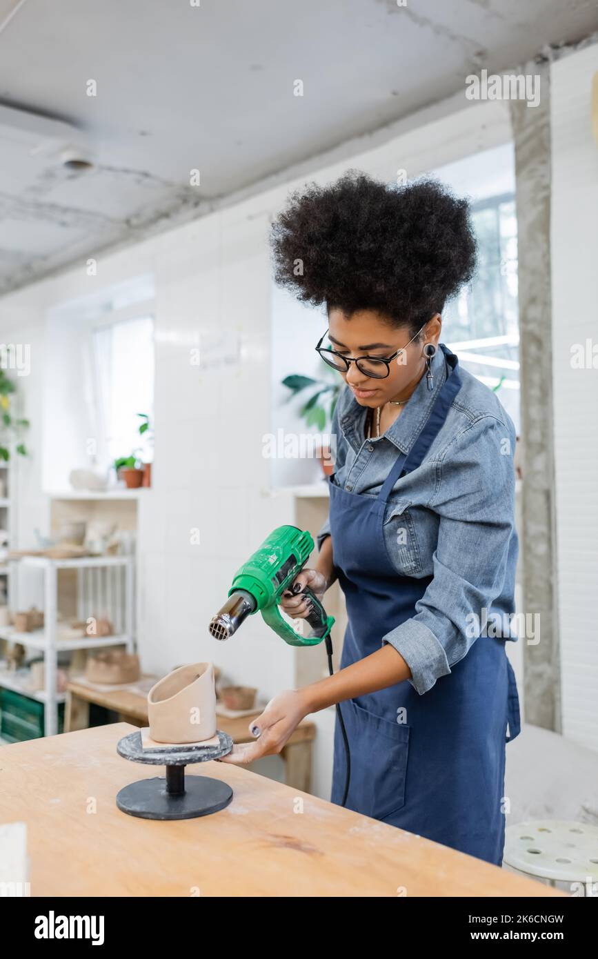 African american craftswoman holding heat gun near clay sculpture in