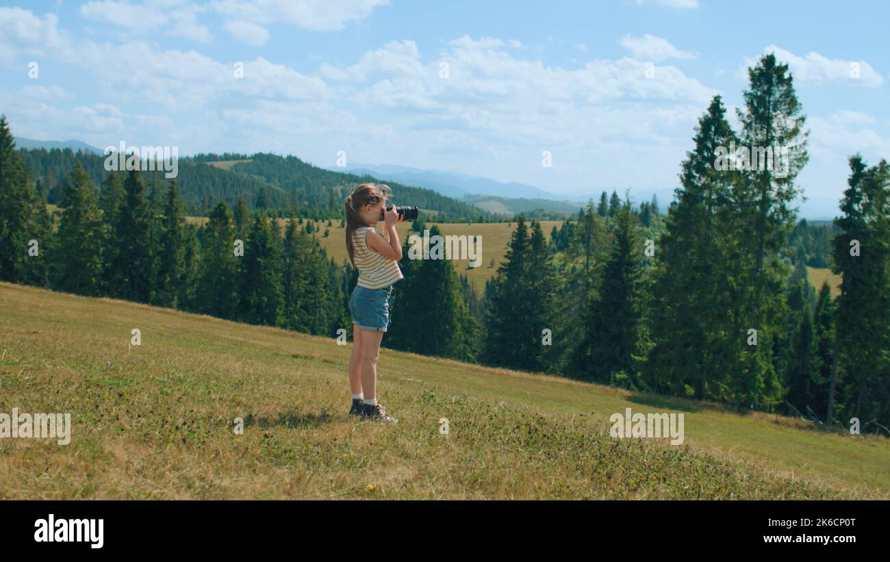 Young photographer shooting landscape on beautifull green hillway, taking pictures of nature. Girl filling the portfolio with amazing photos, spending leisure time outdoor. Slow motion. Stock Photo