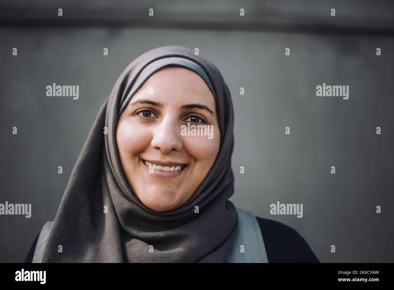 Portrait of smiling female construction worker wearing headscarf against wall Stock Photo