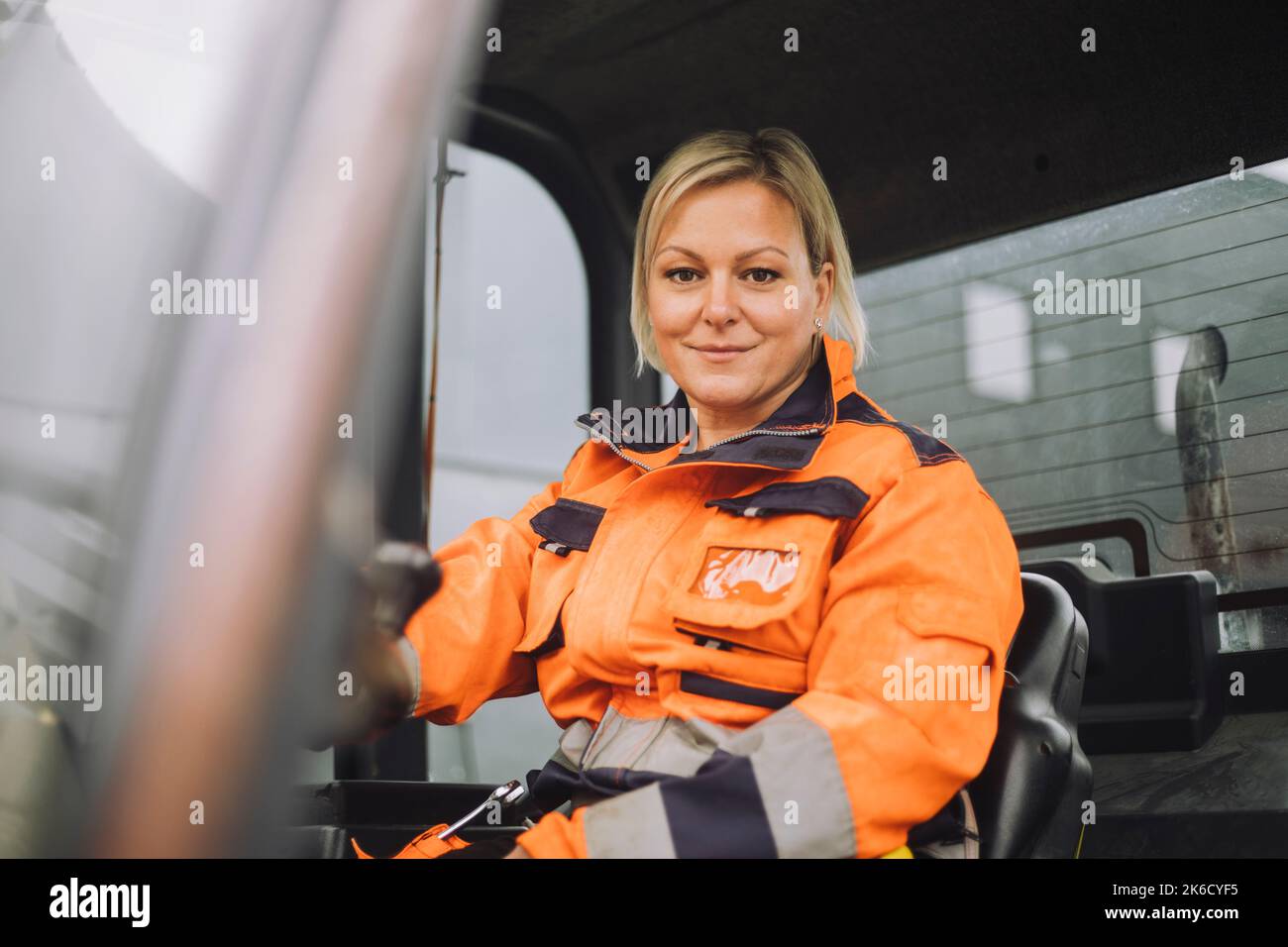 Smiling female construction worker in reflective clothing sitting in vehicle Stock Photo