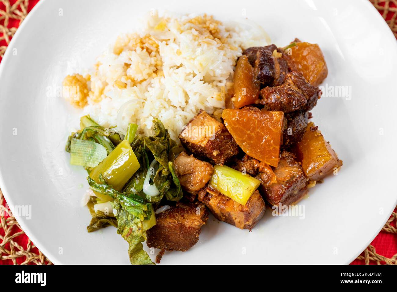 Cube of roasted pork belly, stewed cabbage and kohlrabi and rice on white plate. Vietnamese food, closeup. Stock Photo
