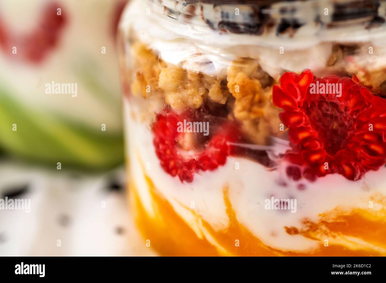 Detailed view to colorful jar with raspberry, granola, nut, joghurt, mango cream and chocolate, blurred second jar with pistachio cream. Stock Photo