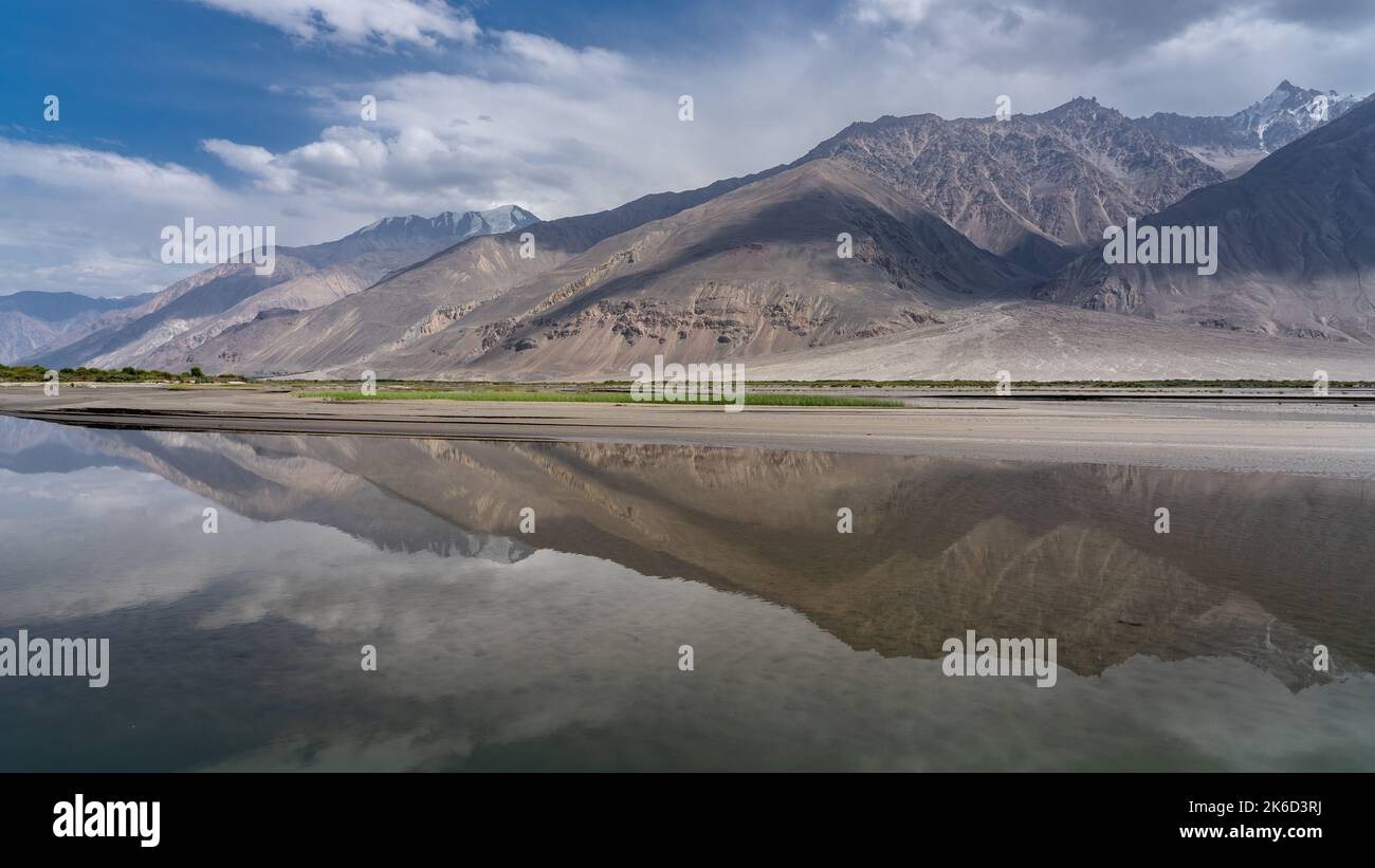 Panorama view of the Wakhan Corridor in Tajikistan Pamir mountains looking towards the Hindu Kush range in Afghanistan with reflection into Panj river Stock Photo