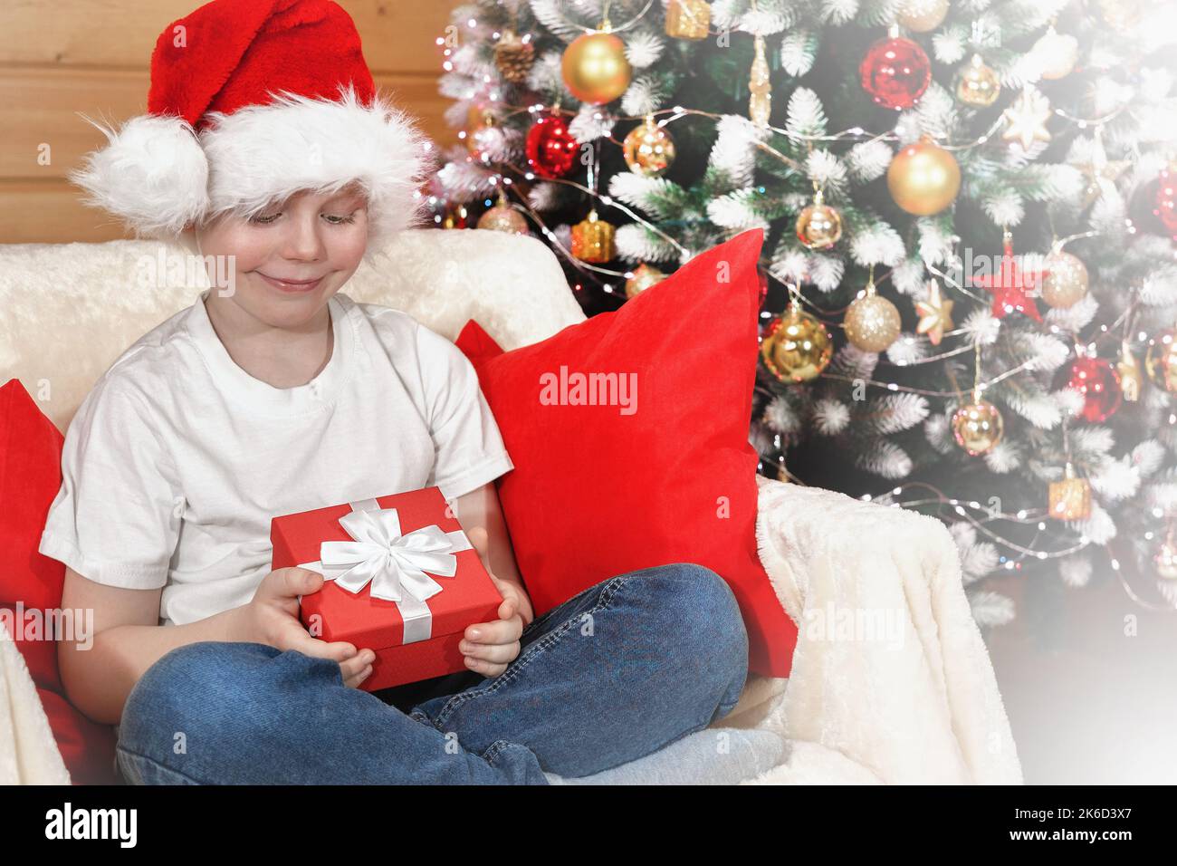 Merry Christmas kids. Emotions of a child. Joyful surprised kid boy in Santa's hat opened a Christmas box with a gift from Santa Claus near the Christ Stock Photo