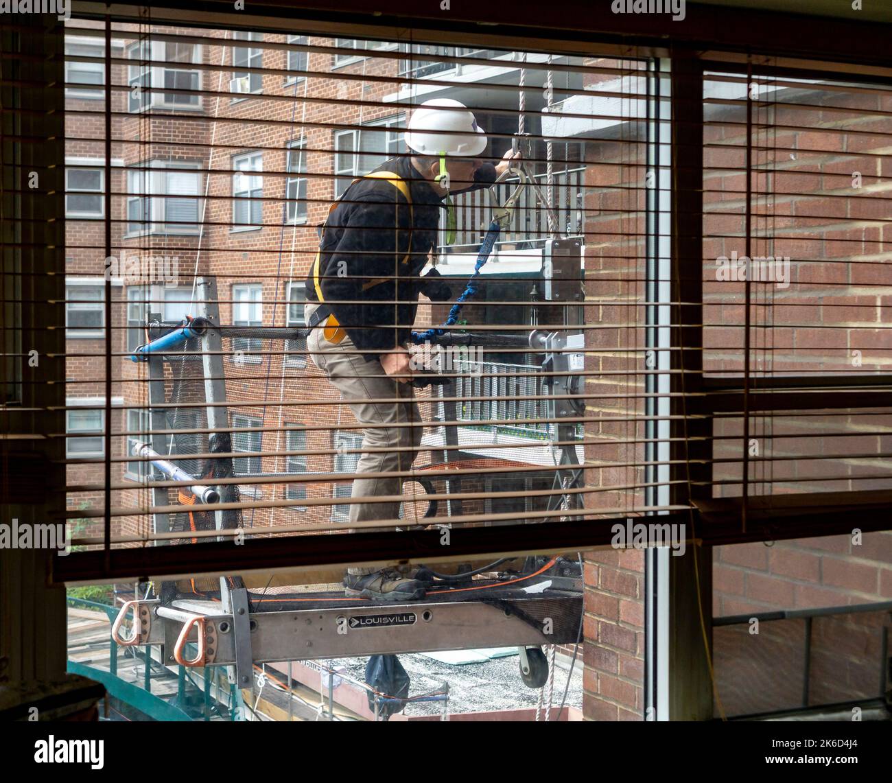 Worker on scaffolding performs citymandated facade inspection and repair on the exterior of an