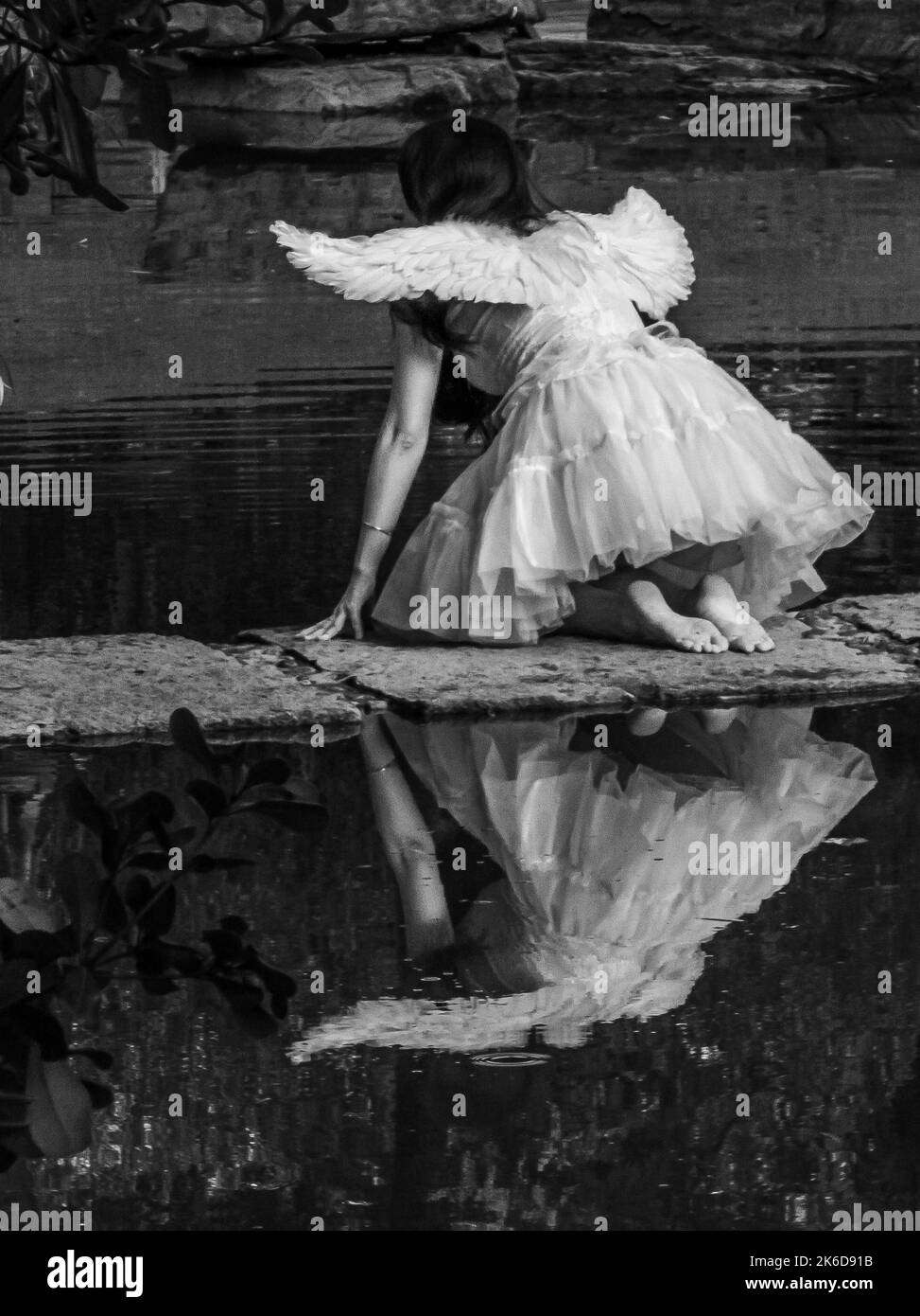 A monochrome shot of a girl in an angel costume reflected on the water Stock Photo