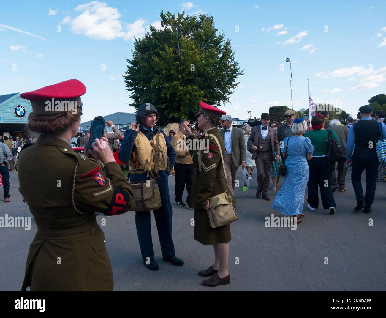 Two women dressed in ATS uniform, one taking a photo of the other next to a man in WW2 RAF uniform, Revival Meeting, Goodwood motor racing circuit, UK Stock Photo