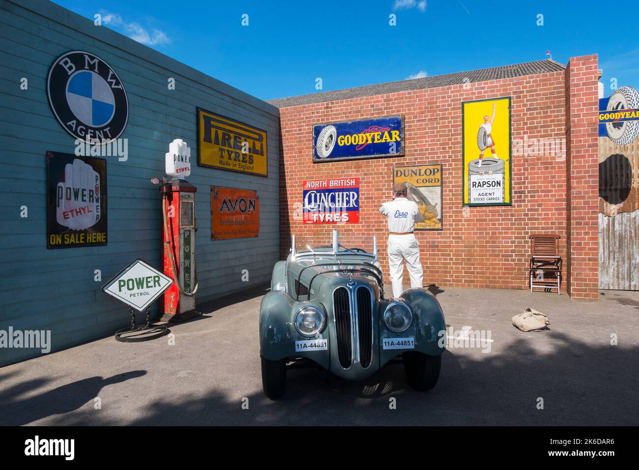 Frazer Nash BMW car parked next to a wall of  authentic car advert signs at the BARC Revival Meeting, Goodwood motor racing circuit, Chichester, UK Stock Photo