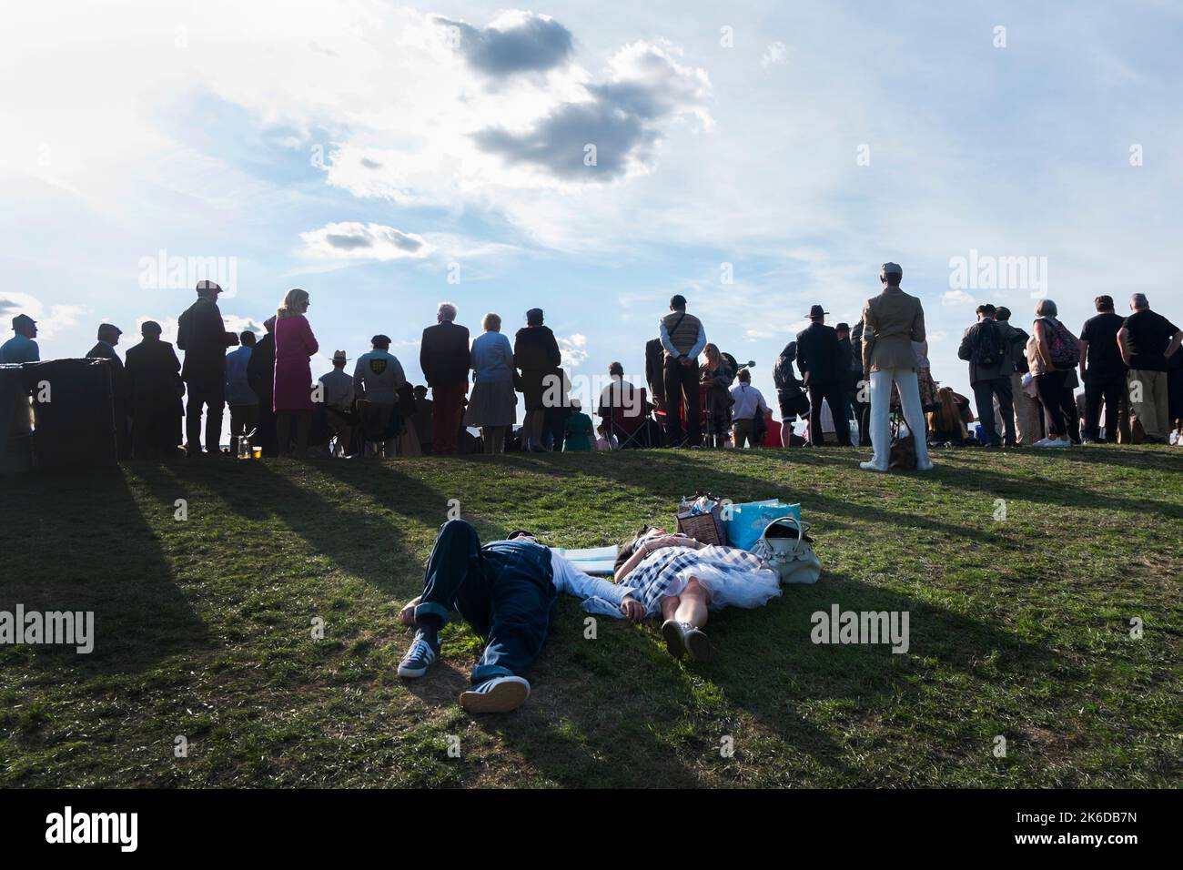 A couple in 1950s attire lying on the grass bank, sleeping while spectators watch the racing, BARC Revival Meeting, Goodwood motor racing circuit, UK Stock Photo