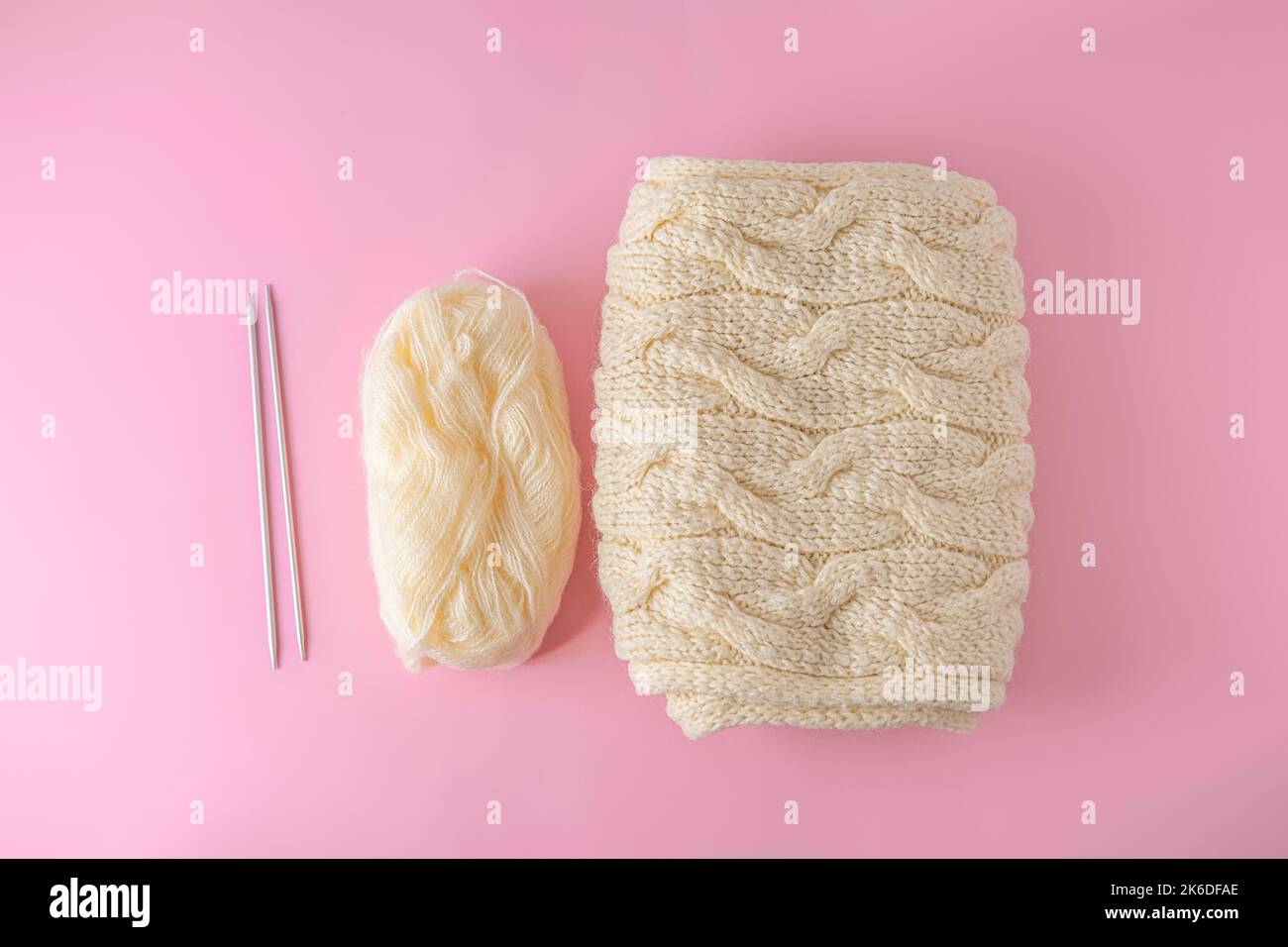 Flat lay with ball of yarn, needles and knitted scarf on light pink background. Handmade and knitting hobby concept Stock Photo