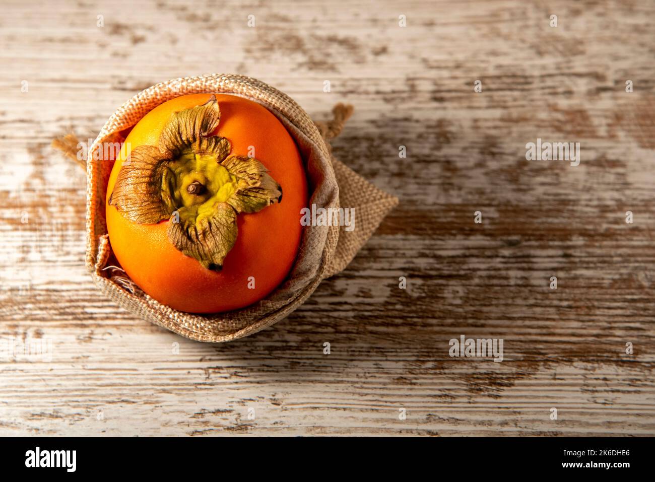 Overhead view of persimmon in burlap sack on weathered white wood Stock Photo