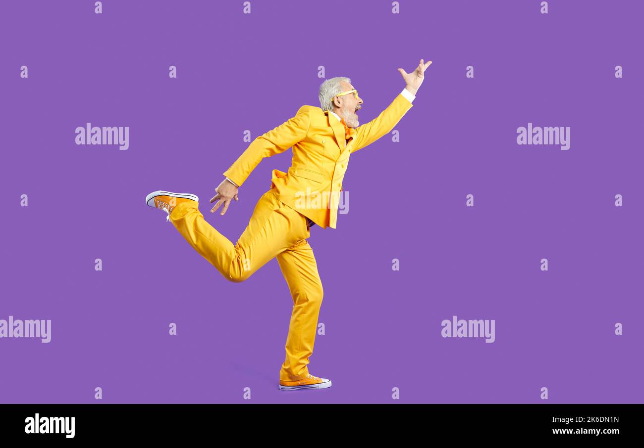 Funny senior man in yellow suit singing and dancing isolated on purple background Stock Photo