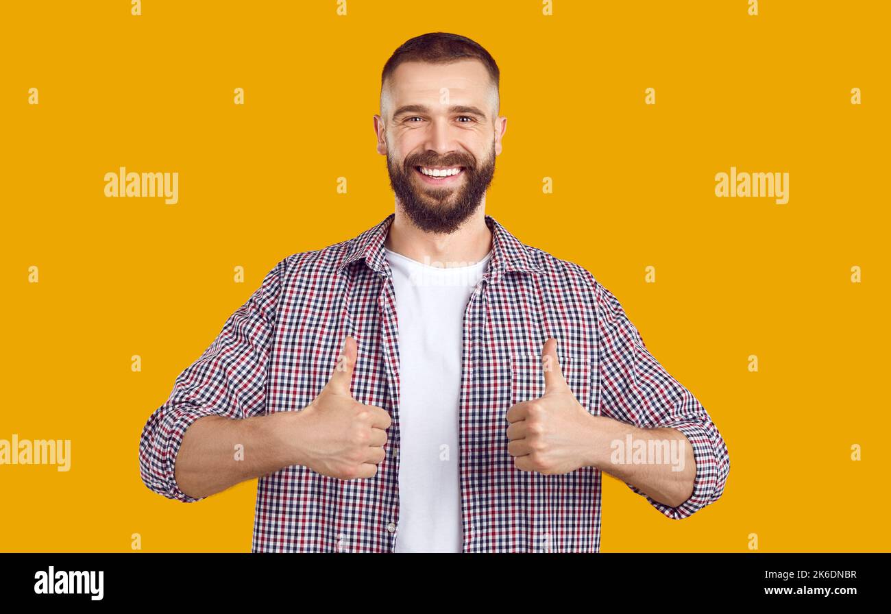 Happy young man in casual clothes smiling and showing thumbs up with his both hands Stock Photo