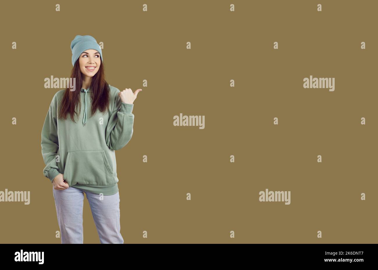 Happy woman in casual wear pointing to side at greenish brown copy space background Stock Photo