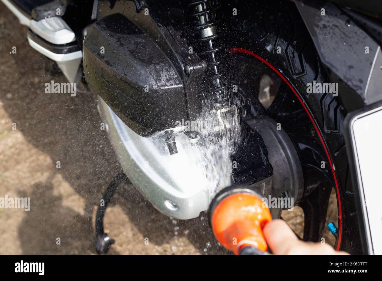 A man washes a motorbike with water from a hose. Maintenance and care