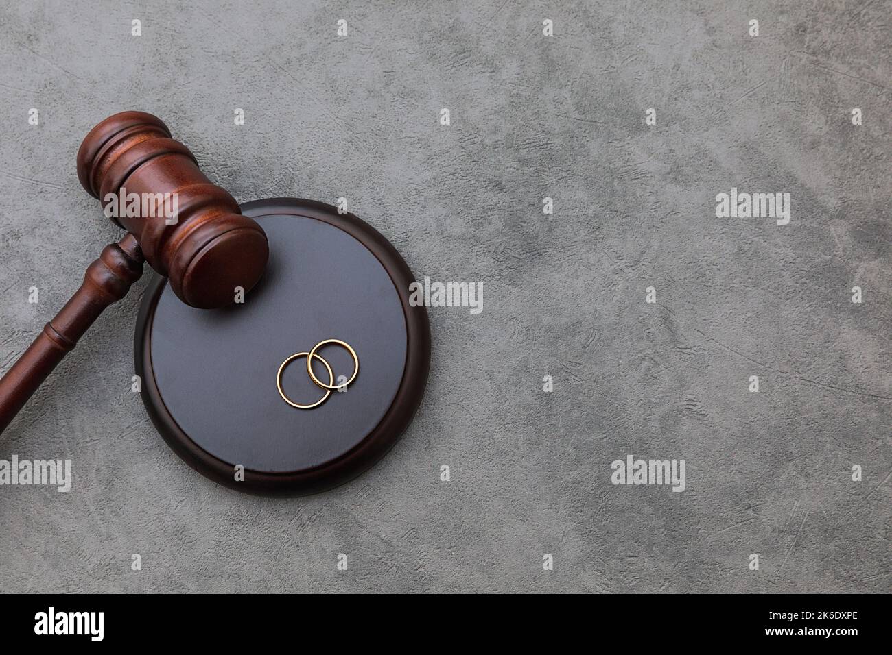Law theme. Judge gavel wedding rings on concrete stone grey background