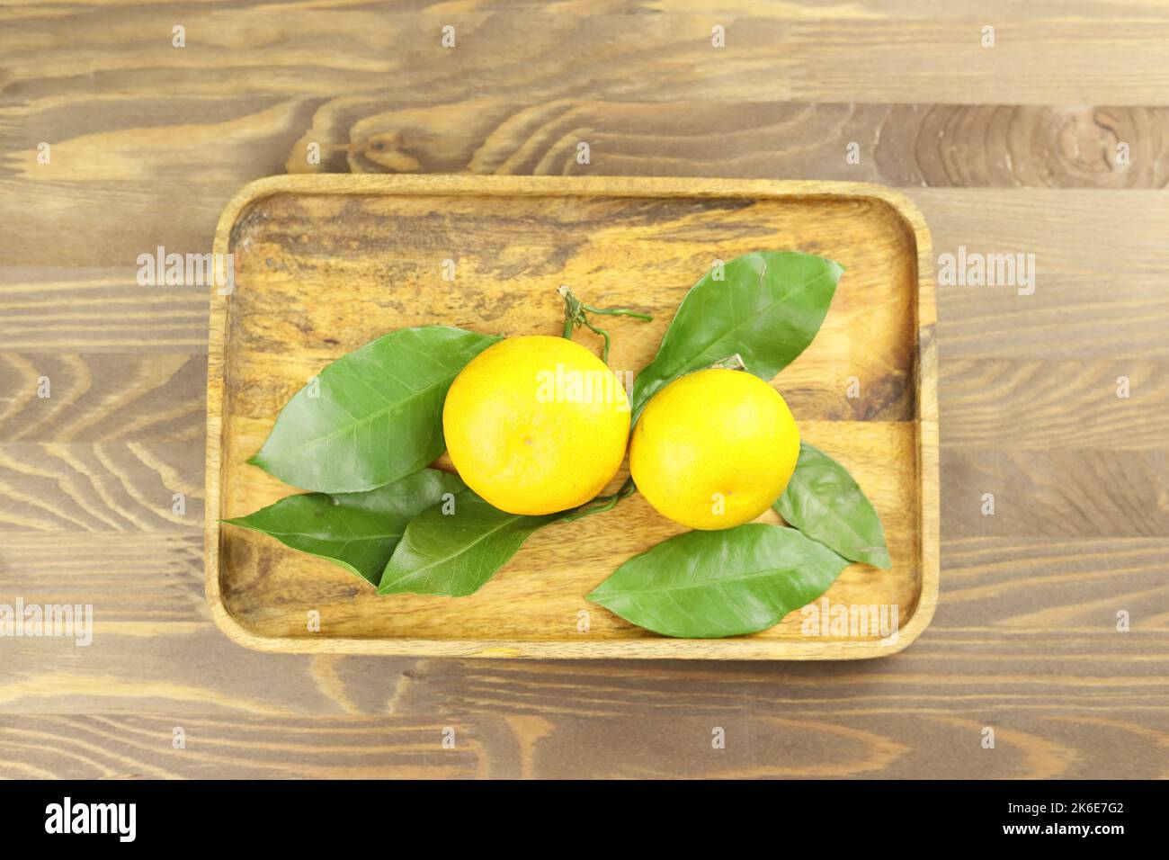 Yellow whole mandarins or tangerine fruits on green leaves on wooden tray. Close-up. Stock Photo