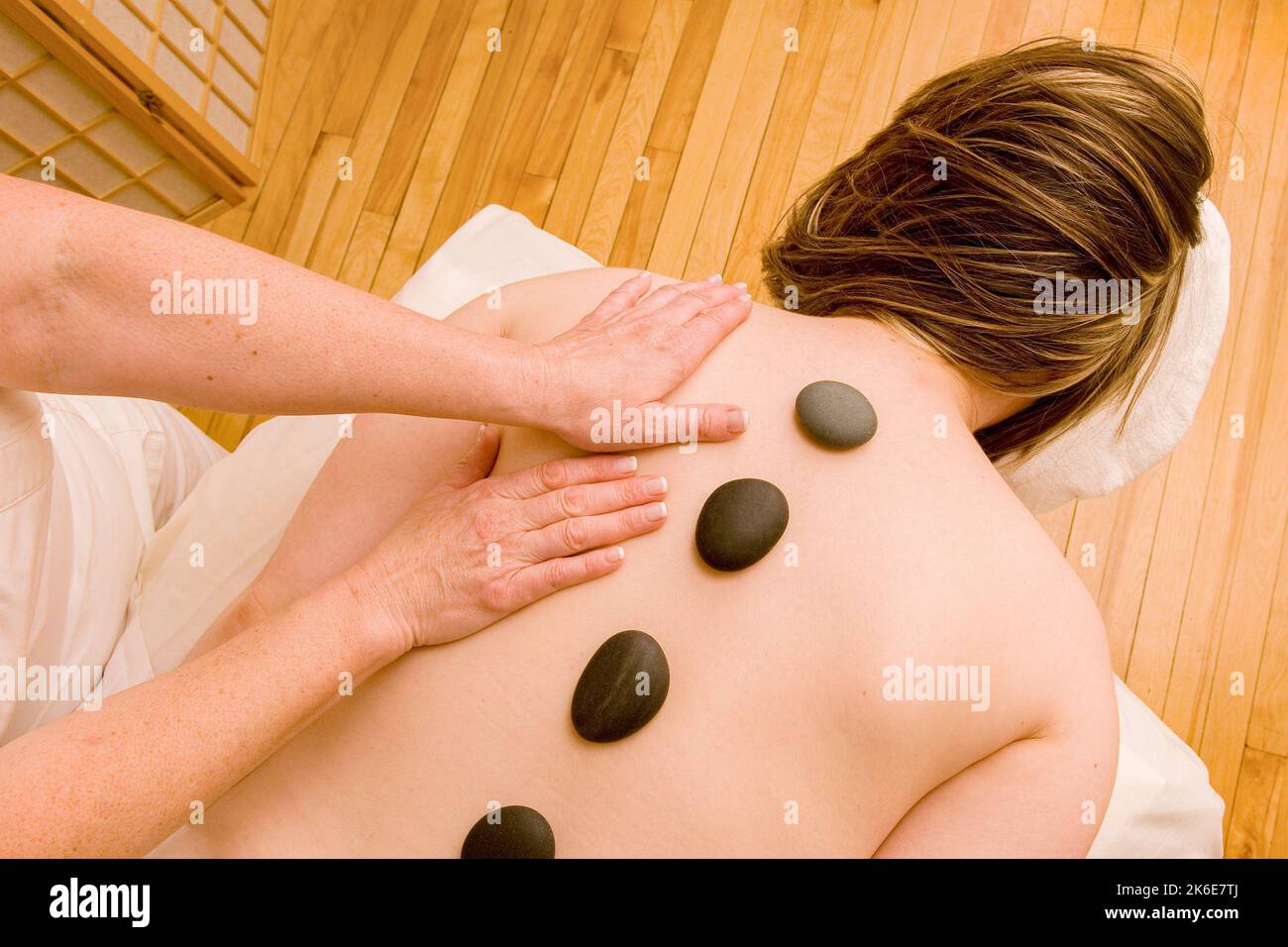 A woman lying on a massage table with small rocks and being massaged Stock Photo