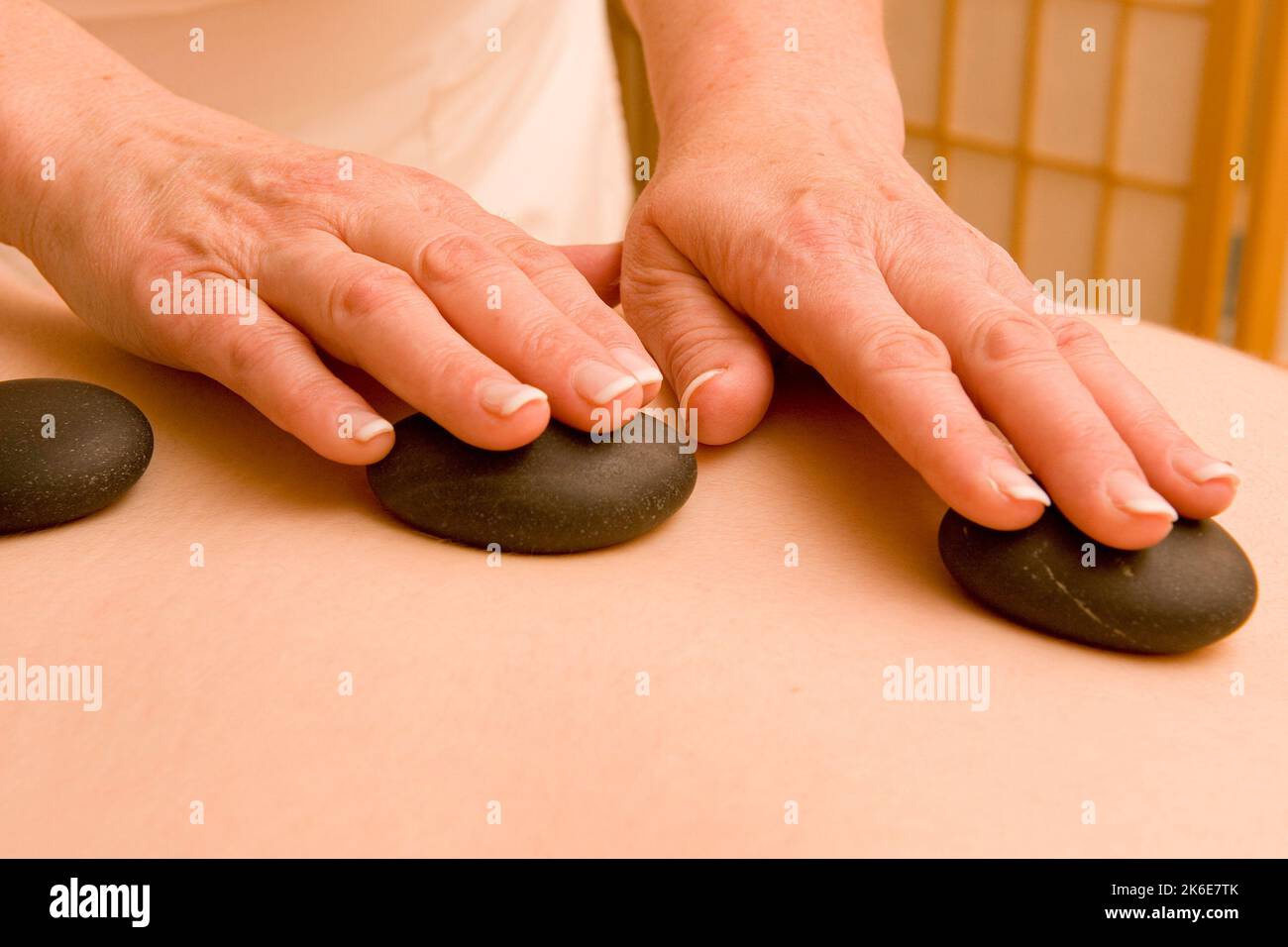 A person lying on the massage table being massaged by rocks placed on their back Stock Photo