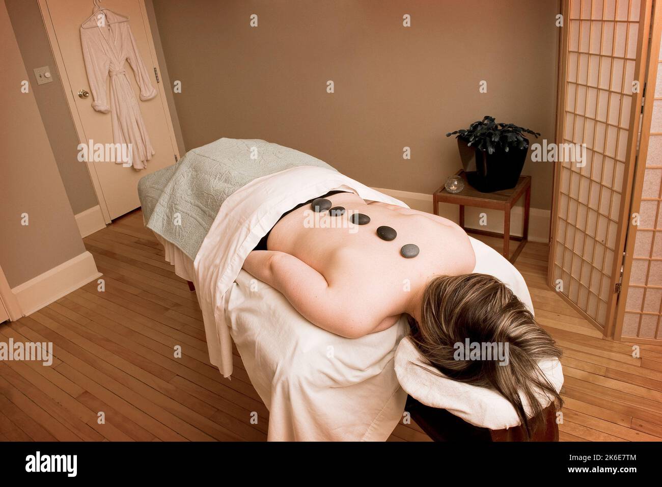 A woman lying on a massage table with small rocks placed on her back Stock Photo