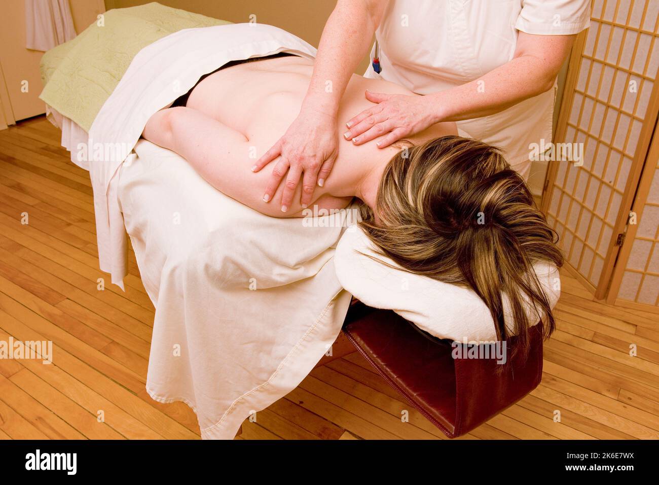 A woman lying on a massage table with small rocks and being massaged Stock Photo
